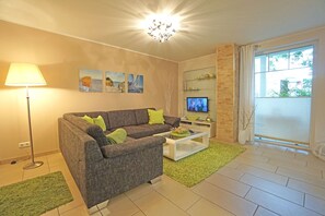 A living room with a grey sofa, green cushions, a white coffee table, a floor lamp, and a TV on a stand.