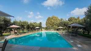 A rectangular swimming pool with clear blue water, surrounded by tiled flooring and shaded by umbrellas. - Casa Vega D: A welcoming cottage in the characteristic style of the Apulian countryside, with Free WI-FI. (San Vito dei Normanni)