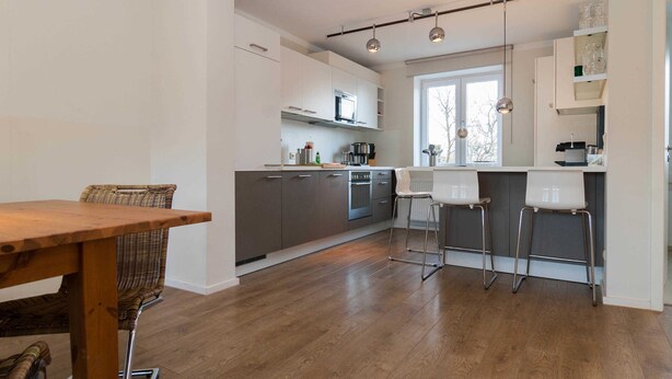 A modern kitchen with a dining area, wooden flooring, and bar stools. - Haus Düne 9, Deutschland (Hörnum (Sylt))