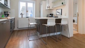A modern kitchen with a central island, bar stools, a window, and a radiator. - Haus Düne 9, Deutschland (Hörnum (Sylt))