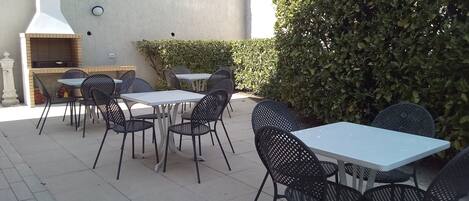 Un patio al aire libre con mesas y sillas, una parrilla y una pared con chimenea.