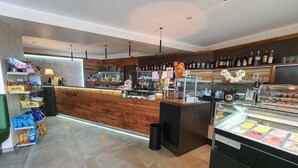 Un área de bar moderna con una barra de madera, estantes llenos de botellas de licores y una vitrina con helados.