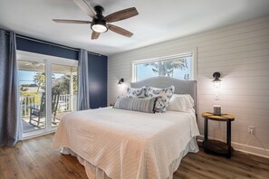 A bedroom with a bed, a ceiling fan, a window with a view, and a balcony.