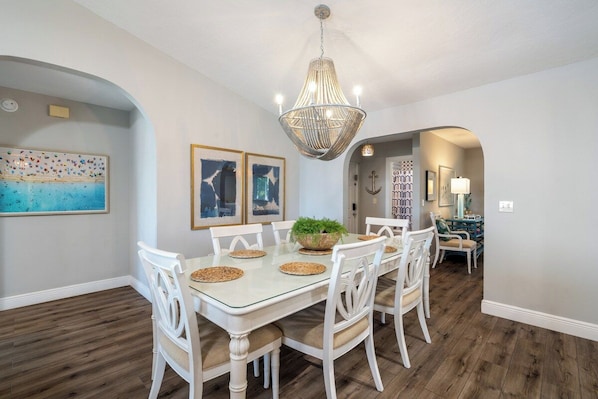 A dining area with a glass table, white chairs, a woven centerpiece, and a hanging light fixture.