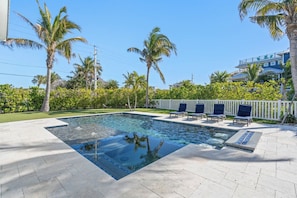 A swimming pool with clear water, surrounded by palm trees and a deck with lounge chairs.