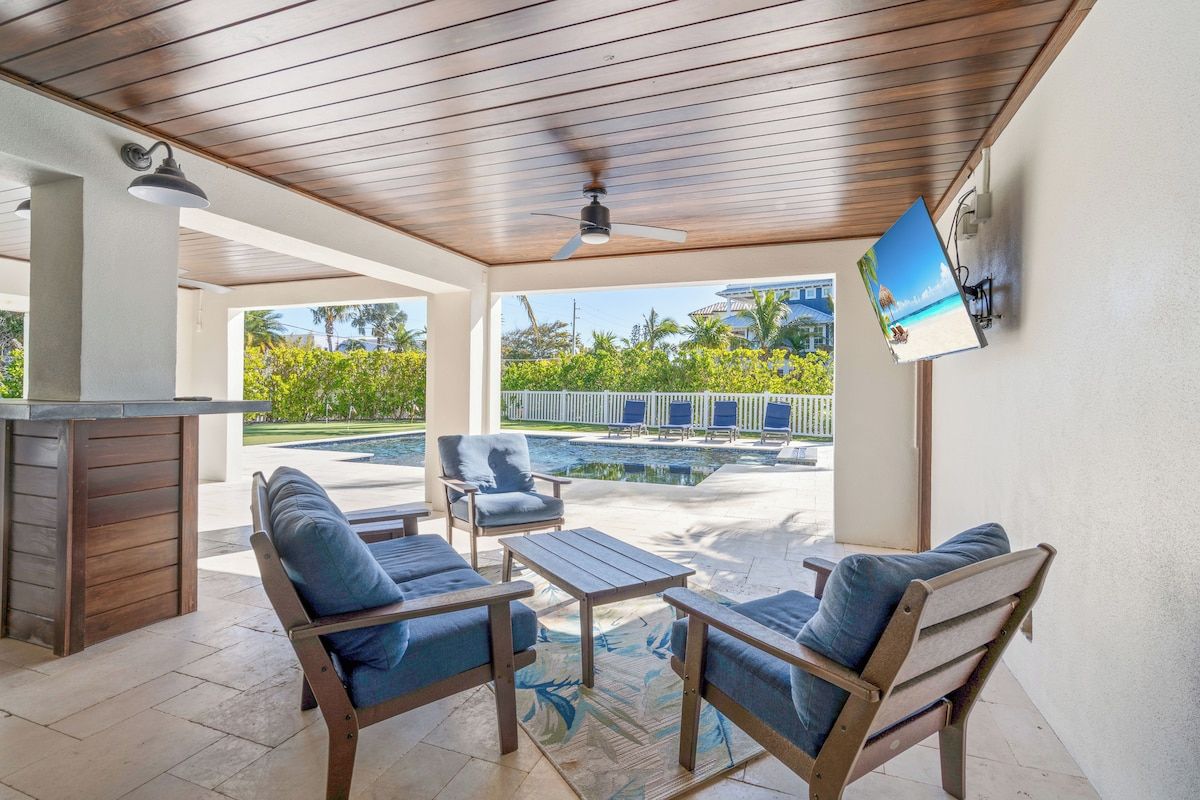 An outdoor patio with wooden furniture, a pool, and a view of a resort.