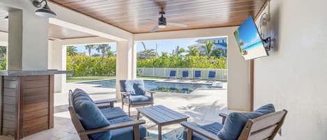 An outdoor patio with wooden furniture, a pool, and a view of a resort.