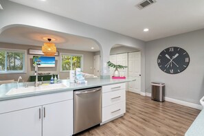 A modern kitchen with a built-in dishwasher, a large clock on the wall, and a view of the outdoors through the windows.