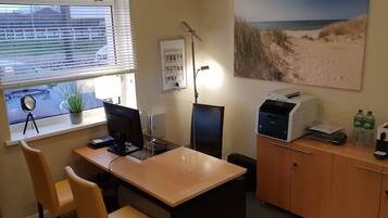 Ein Homeoffice mit Schreibtisch, Computer, Drucker und einem Fenster mit Jalousien.