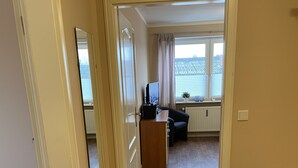A hallway leading to a living area with a wooden floor, a television, and a window with curtains. - Airport Hotel One (Sylt)
