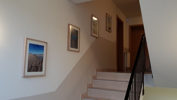 A staircase with a handrail, a wall with three framed pictures, and a light fixture on the left. - Airport Hotel One (Sylt)