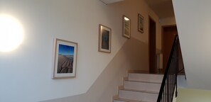 A staircase with a handrail, a wall with three framed pictures, and a light fixture on the left. - Airport Hotel One (Sylt)
