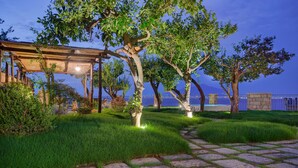 A stone pathway leading to a wooden pergola with a view of a blue building in the background. - Villa Galidia with Jacuzzi, Sea View, Garden and Air Conditioning (Sorrento)