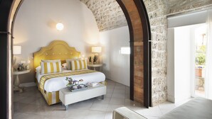 A hotel room with a large bed, a bedside table, a lamp, and a view through an arched doorway. - Villa Galidia with Jacuzzi, Sea View, Garden and Air Conditioning (Sorrento)
