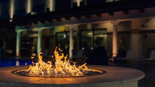 A circular outdoor fire feature with flames, surrounded by a pool and a building with columns and glass windows in the background. - Hotel Indigo Spring - Woodlands Area by IHG (Spring)