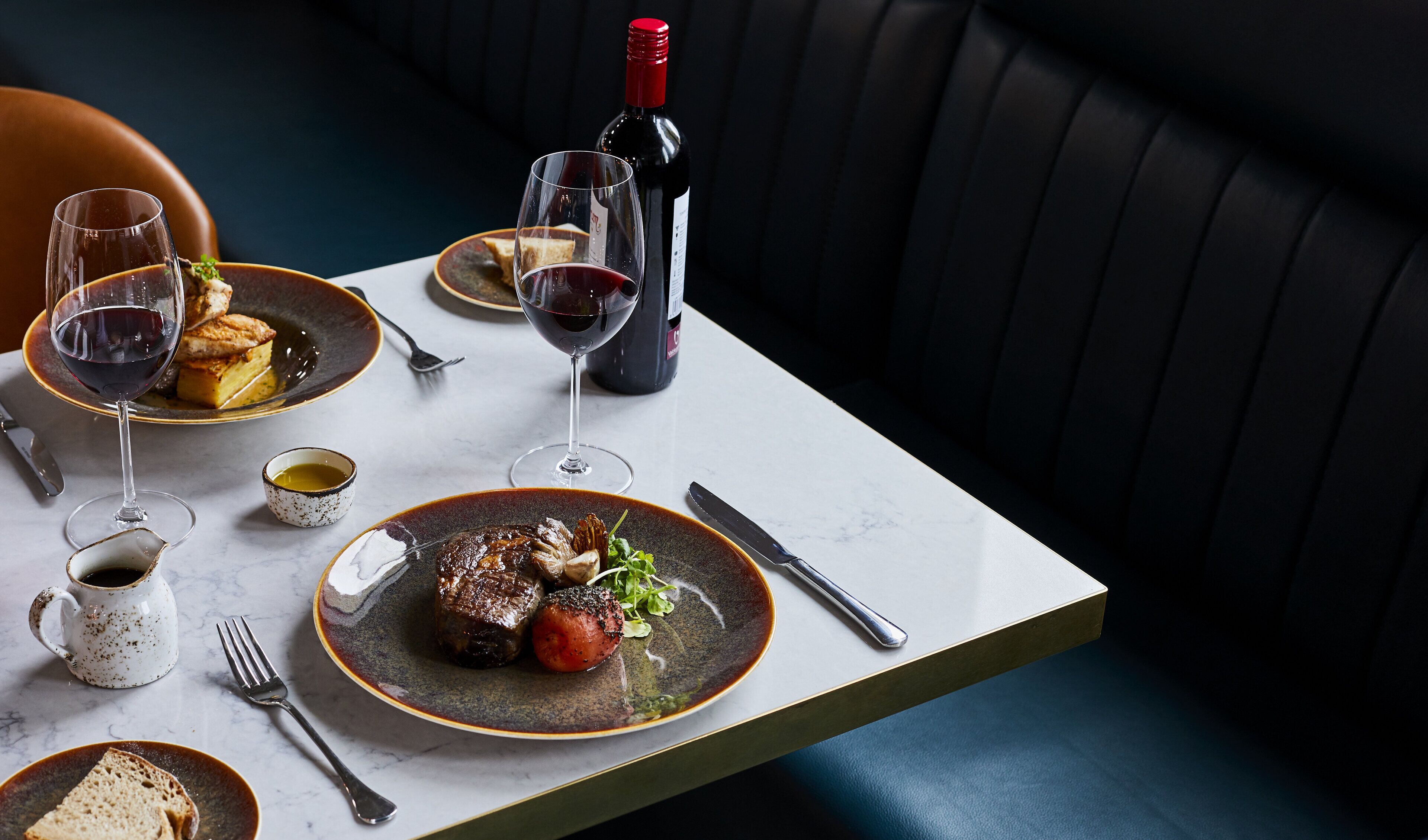 Una mesa de comedor con platos de comida, copas de vino y cubiertos.