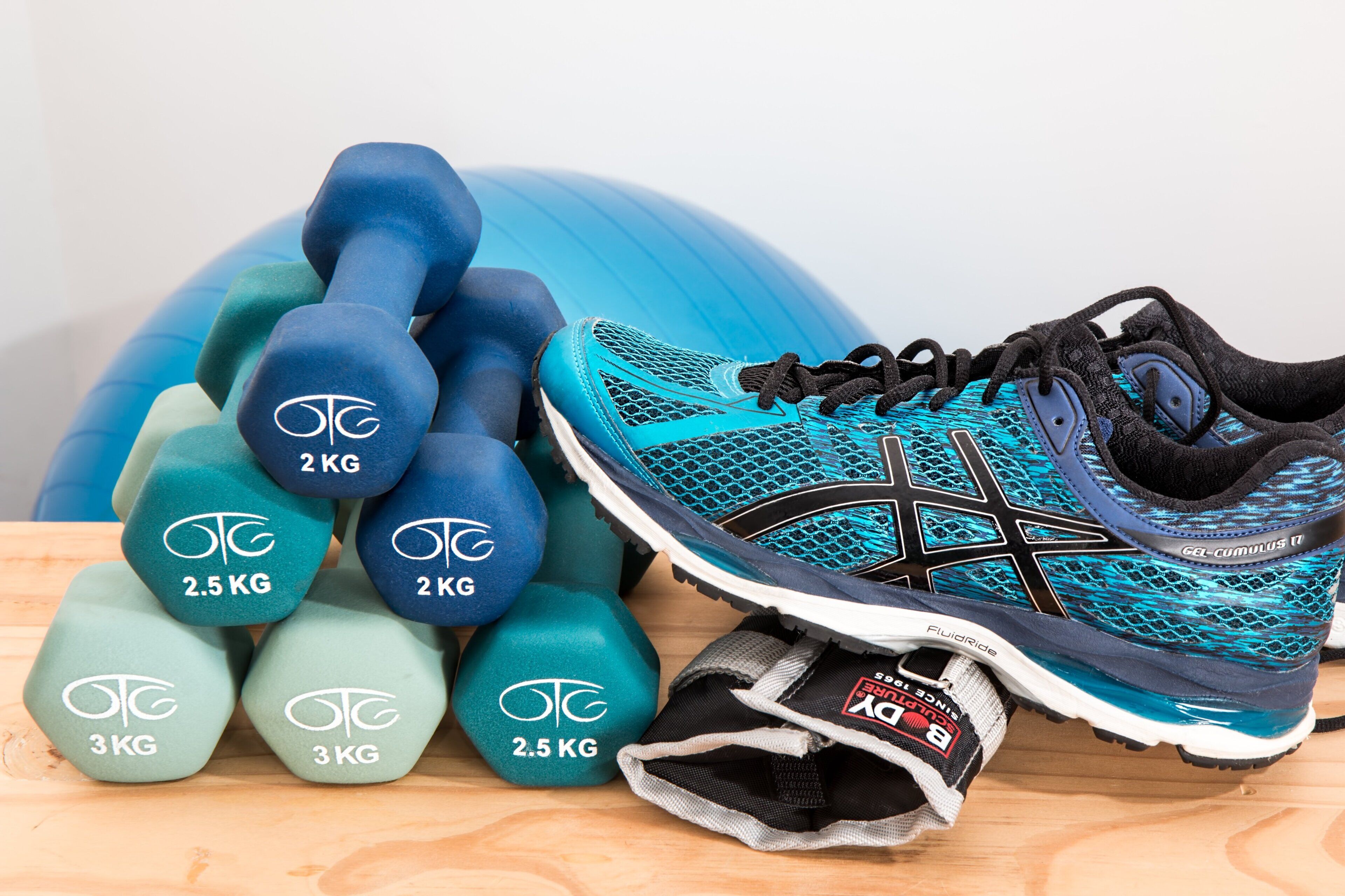 A pair of athletic shoes, a set of dumbbells, and a blue exercise ball.