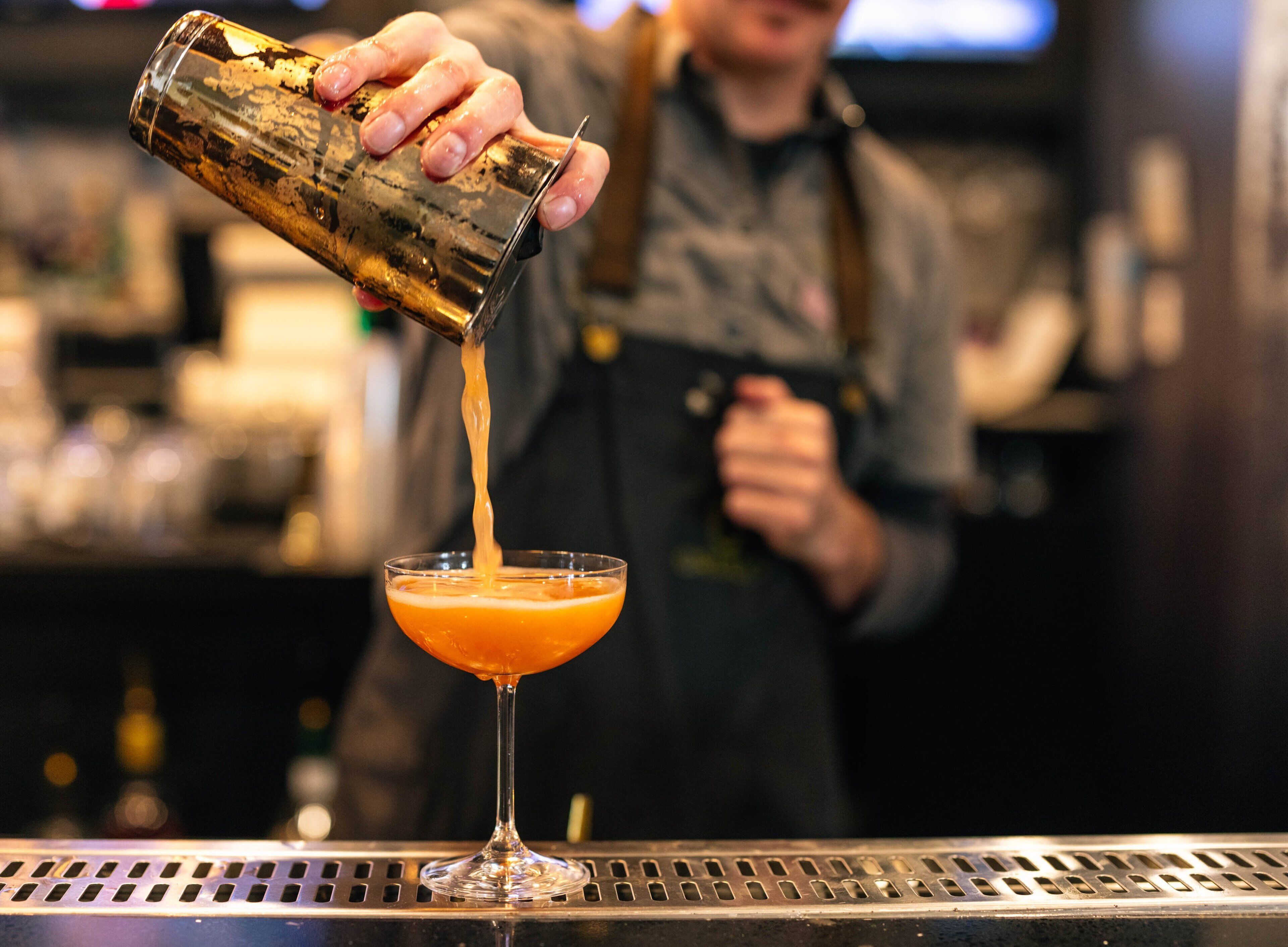En bartender som häller upp en drink i ett martiniglas.