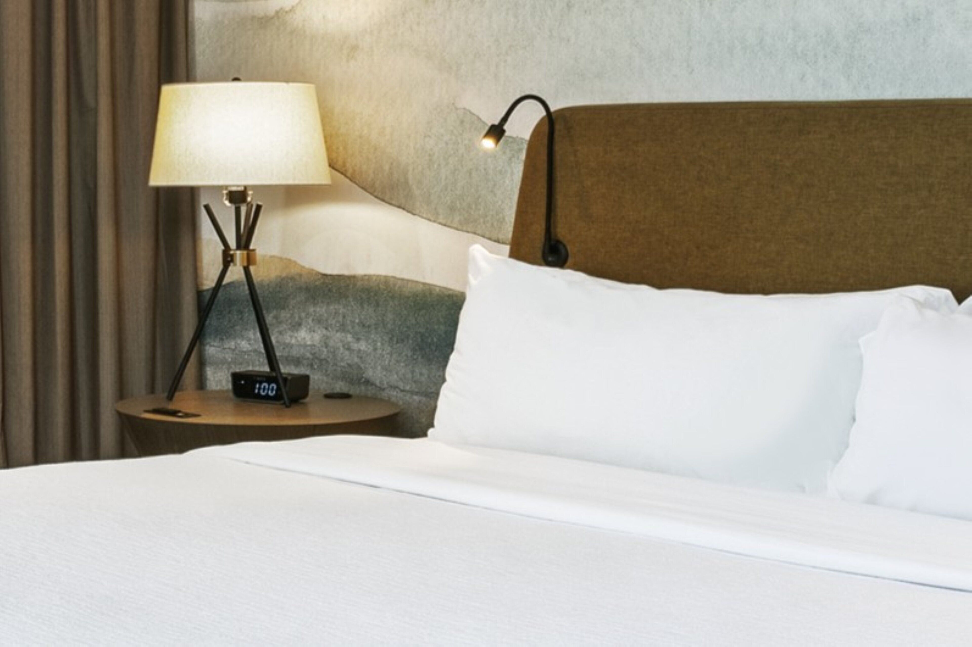 A hotel room with a bed, a bedside table with a lamp, and a digital clock.