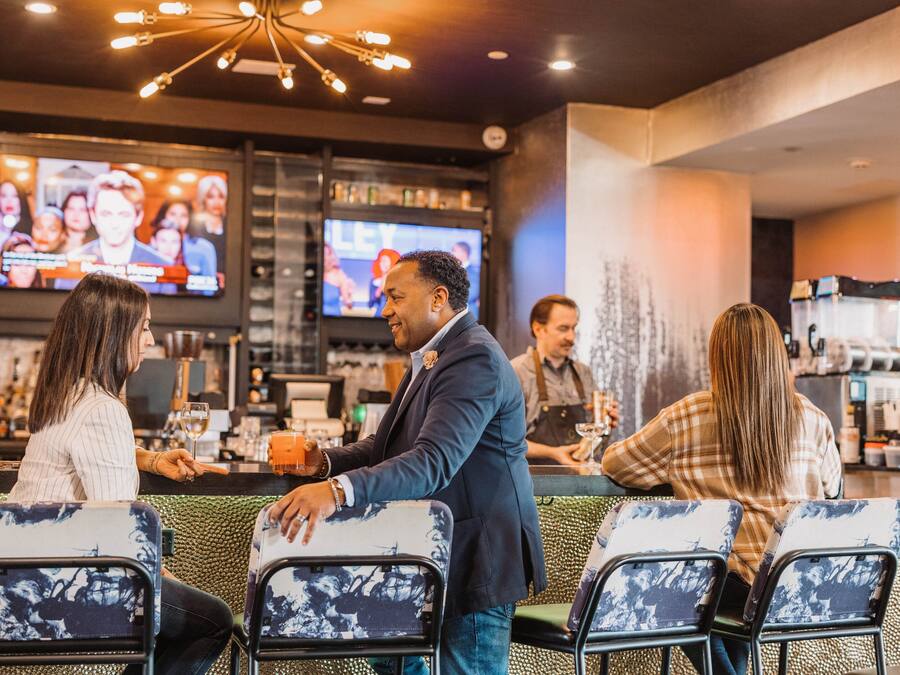 Un espace bar avec des sièges, un téléviseur diffusant des programmes sportifs et un comptoir où travaille un barman.