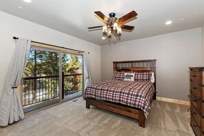 Un dormitorio con una cama, un ventilador de techo, un aparador y un ventanal con vistas a árboles.