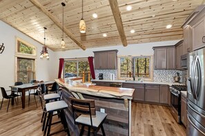 Una cocina moderna con vigas de madera, una isla central, taburetes de bar y un refrigerador de acero inoxidable.