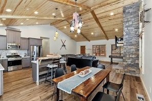A spacious kitchen with modern appliances, a dining area with a wooden table, and a stone fireplace. - Luxury NEWLY Built Single Story Log Cabin! 4 BR 3 Bath! Highly Desired Fox Farm Location! GAME TABLE! Short Drive to Resorts, Lake, and Big Bear Village! (Big Bear Lake)