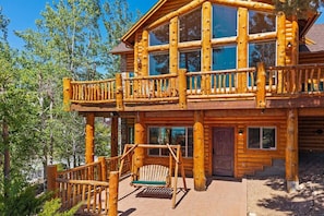 A log cabin with a balcony, a swing, and a wooden deck.