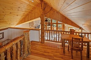 Ein Holzinnenraum mit hoher Decke, einer Treppe mit einer Geländer aus Naturholz und einem Essbereich mit Tisch und Stühlen.