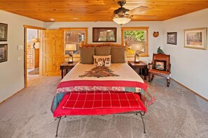 A bedroom with a bed, a ceiling fan, a fireplace, and a door leading to another room. - Log Styling with Spectacular Lake Views! HOT TUB! Wall to Wall Game Room! (Big Bear Lake)