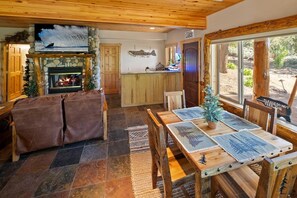Gemütliches Interieur einer Lodge mit Kamin aus Stein, Holzmöbeln und Blick ins Freie.