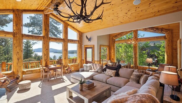 A spacious log cabin with large windows offering views of a lake and mountains.