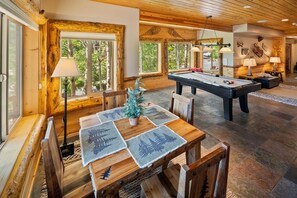 A wooden interior with a pool table, dining table, and chairs.