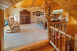 A log cabin interior with a wooden rocking chair, a bed with a rustic headboard, a large wooden cabinet, and a chandelier. - Log Styling with Spectacular Lake Views! HOT TUB! Wall to Wall Game Room! (Big Bear Lake)
