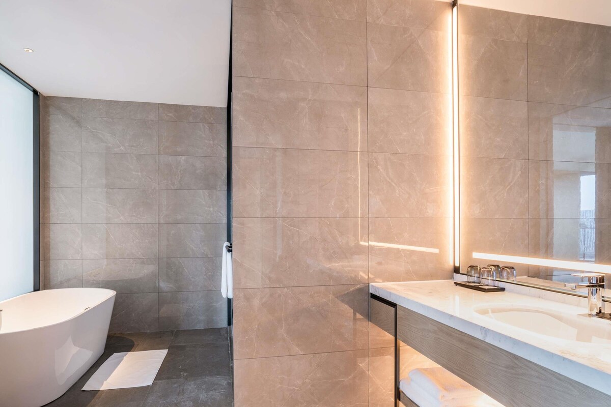 Un baño moderno con una bañera independiente, un espejo grande y una encimera con lavabo y mueble de tocador.