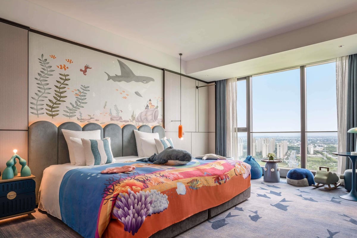 Une chambre à coucher moderne avec un grand lit, une vue sur la ville et une fresque représentant des créatures marines sur le mur.