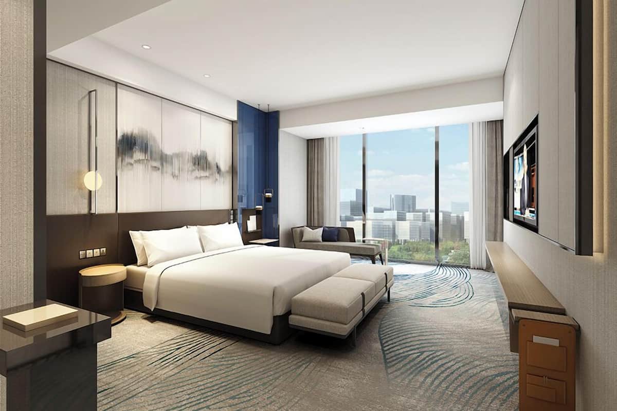 A modern hotel room with a large bed, a desk, a chair, and a view of the city.