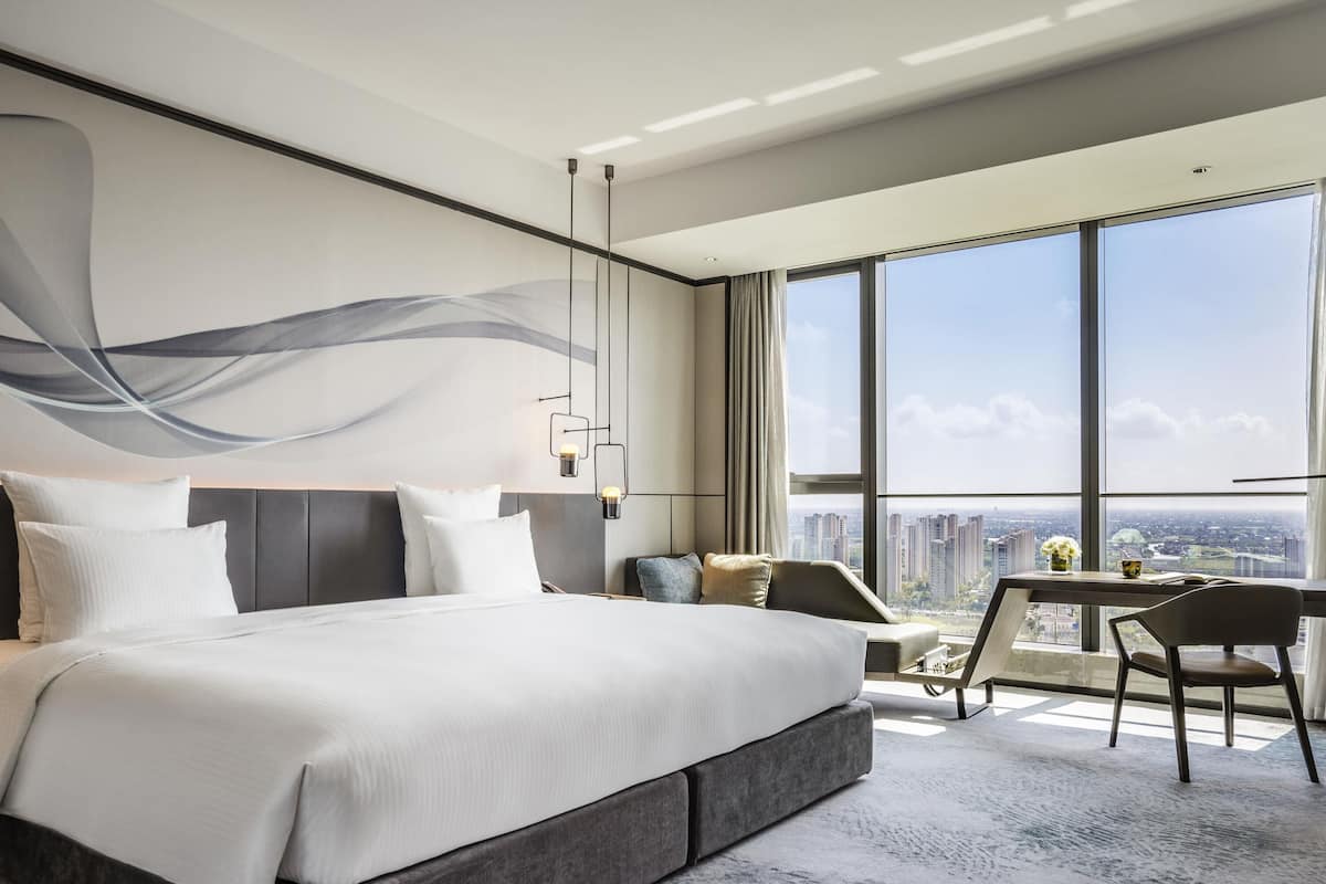 Une chambre d’hôtel moderne, dotée d’un grand lit, d’un bureau et offrant une vue sur le paysage urbain.