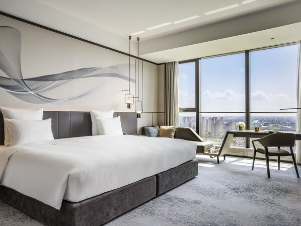 Quarto de hotel moderno com uma cama grande, uma mesa de trabalho e vista para a cidade.