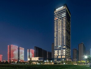 Un hotel de gran altura con un llamativo letrero de 'Pullman', rodeado de otros edificios y un parque bien cuidado.