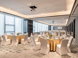 A spacious conference room with multiple round tables, white chairs, and a large screen at the front. - Pullman Jiaxing Pinghu Excellence (Jiaxing)
