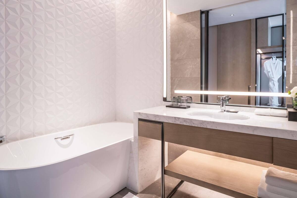 Un baño moderno con una bañera independiente, un espejo grande y un tocador con lavabo y toallero.
