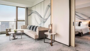 A modern hotel room with a large bed, a sofa, a small table, and a large window offering a city view.