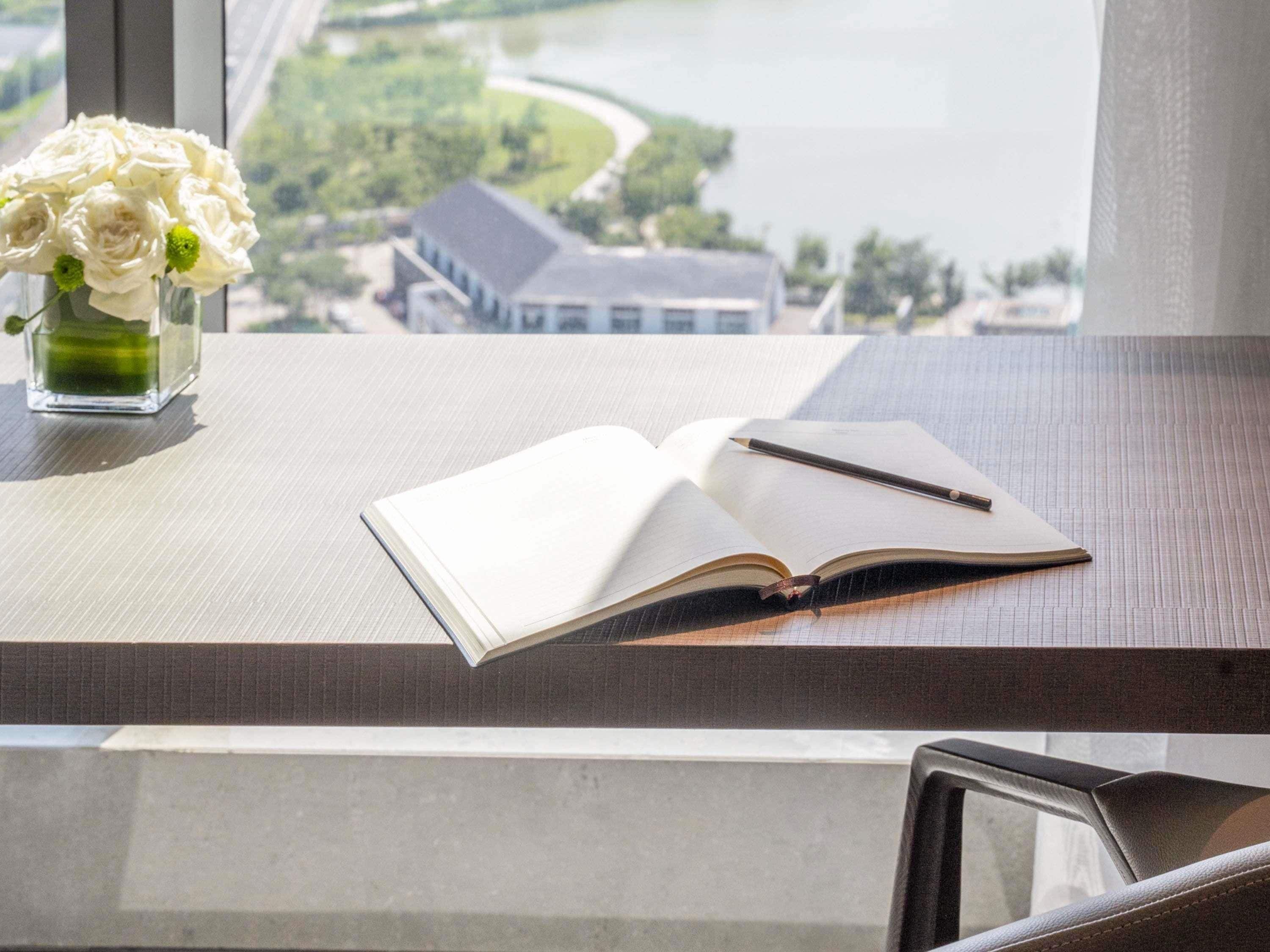 A desk with an open notebook, a pen, and a vase of white flowers.