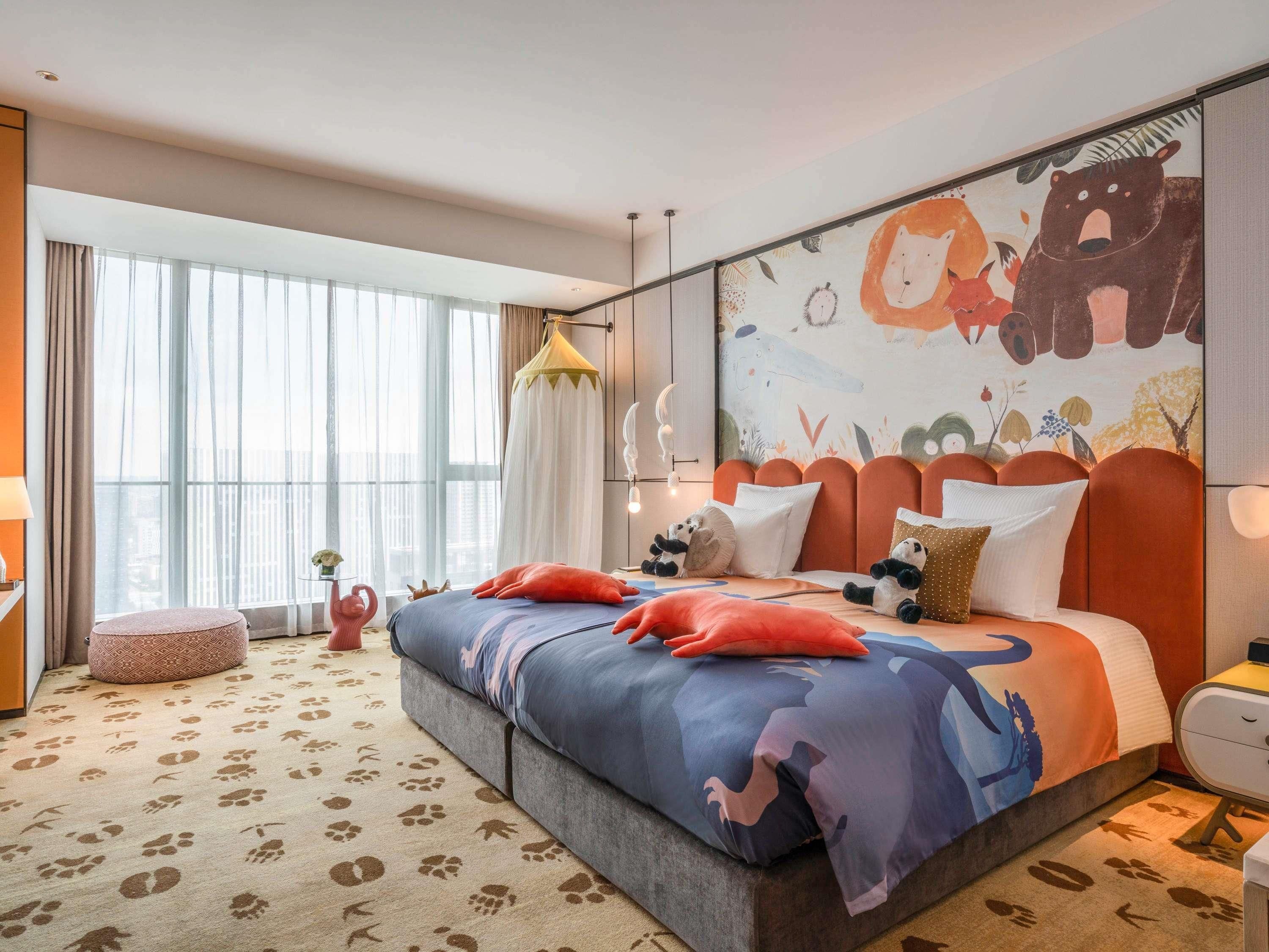 A modern hotel room with a large bed, a colorful mural, and a large window with curtains.