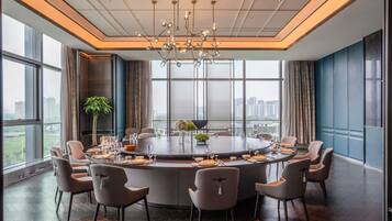 A modern conference room with a round table, multiple chairs, a chandelier, large windows, and a city view.