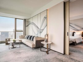 Una habitación de hotel moderna con una cama grande, un sofá, una mesita y un amplio ventanal con vistas a la ciudad.