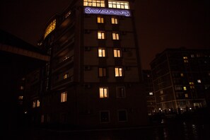 A multi-story building with illuminated windows and a sign reading "SULO APARTMENTS".