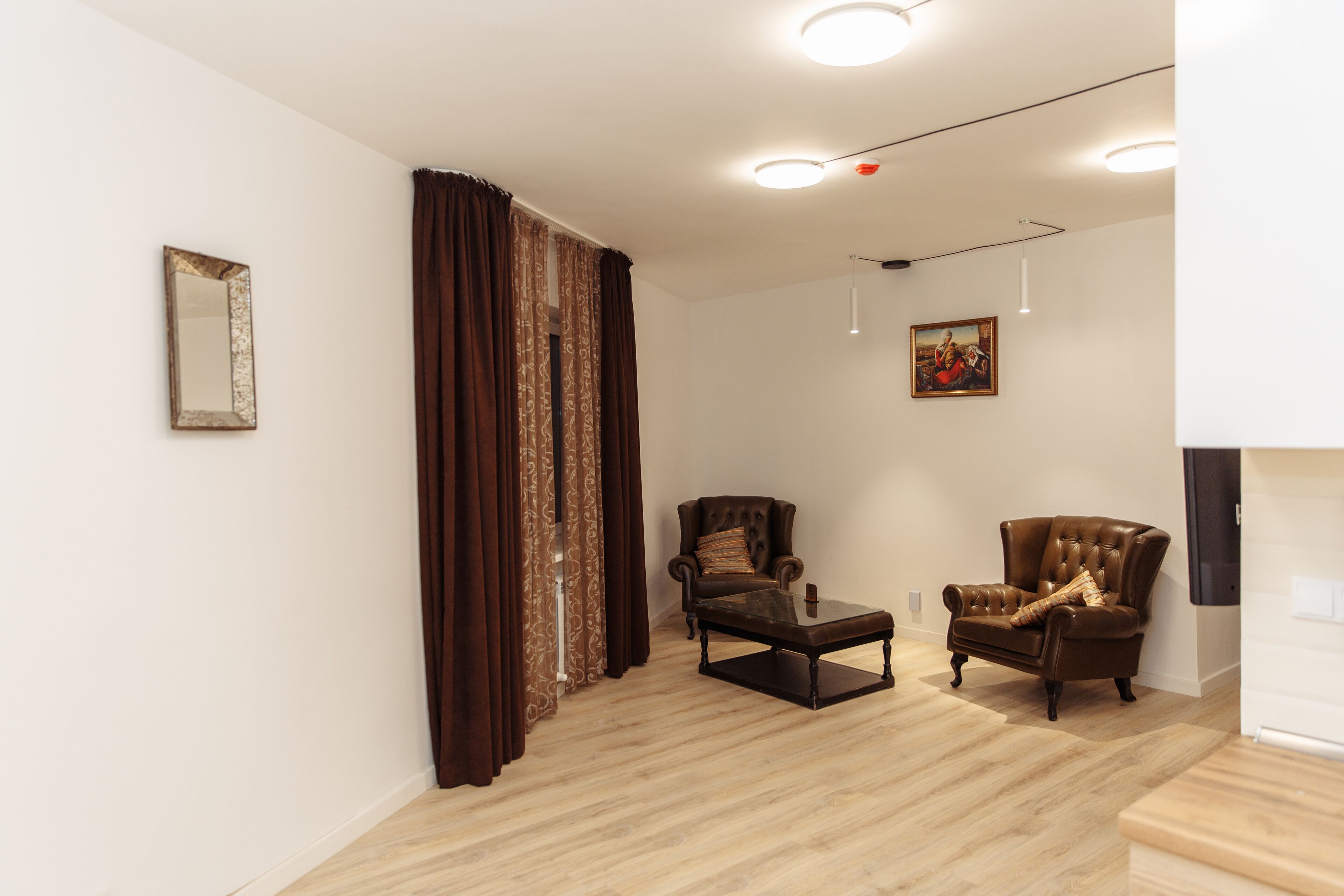 A living room with a brown leather armchair, a matching ottoman, a large mirror, and a painting on the wall.