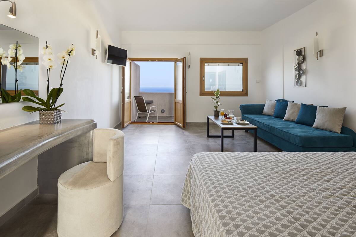 Une chambre d’hôtel moderne dotée d’un balcon, d’un canapé, d’un lit et d’une petite table sur laquelle est posé un vase de fleurs.